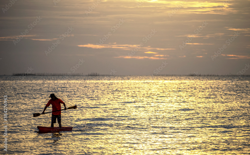 Photo shot of water spatter from fisherman while throwing fishing net from boat. Silhouette of asian fishermen with fishing net in morning sunshine along harbor. Stop motion water drop on sea