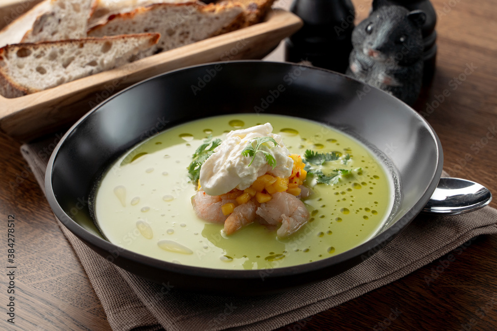 Creamy green soup with crab meat and shrimps on wooden table in a fancy fish restaurant, soft light Creamy green soup with crab meat and shrimps on wooden table in a fancy fish restaurant, soft light