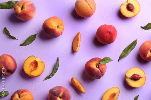Fototapeta Naklejka Na Ścianę i Meble -  Fresh ripe peaches and green leaves on violet background, flat lay