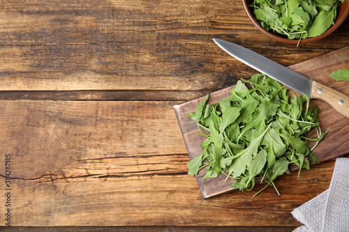 Cutting board with fresh arugula leaves and knife on wooden table, flat lay. Space for text