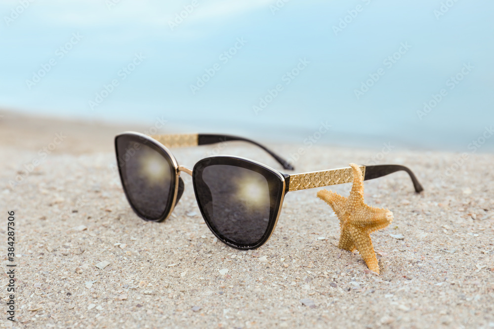Stylish sunglasses and starfish on sandy beach