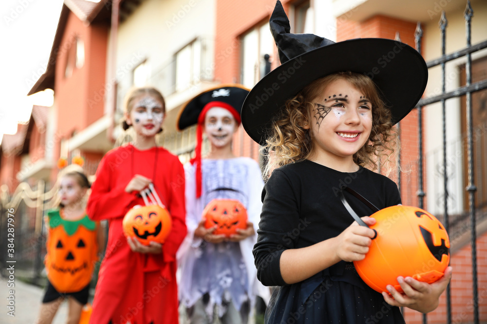 Cute little girl with pumpkin candy bucket wearing Halloween costume outdoors