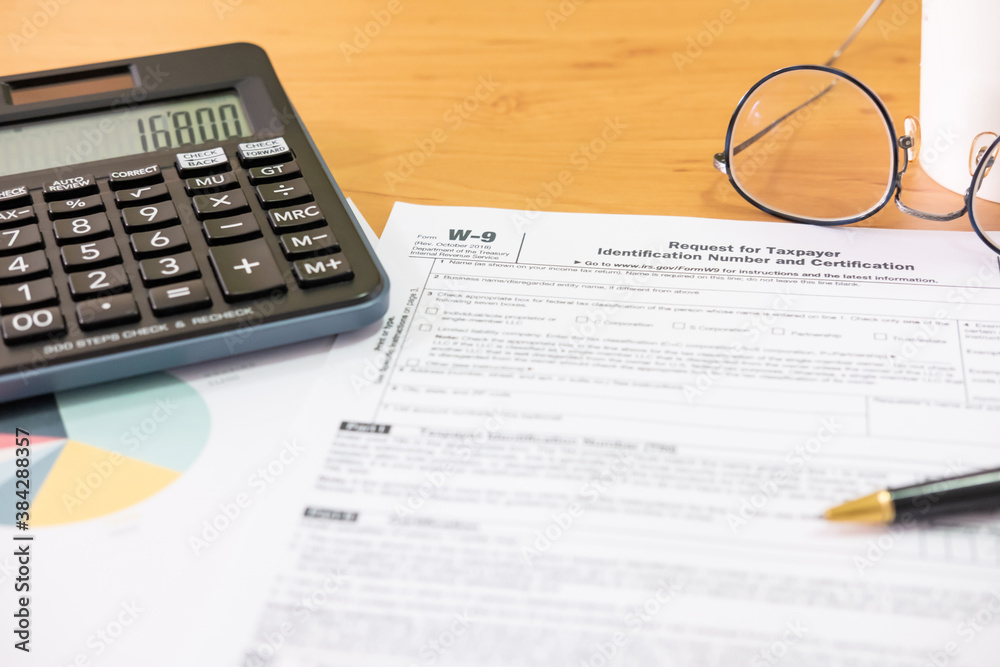 Fototapeta premium Selective focus Calculator button. American US tax form on wooden table. With blurred calculator, pen and glasses. Taxation time obligation for people who has income that need to comply to regulation.