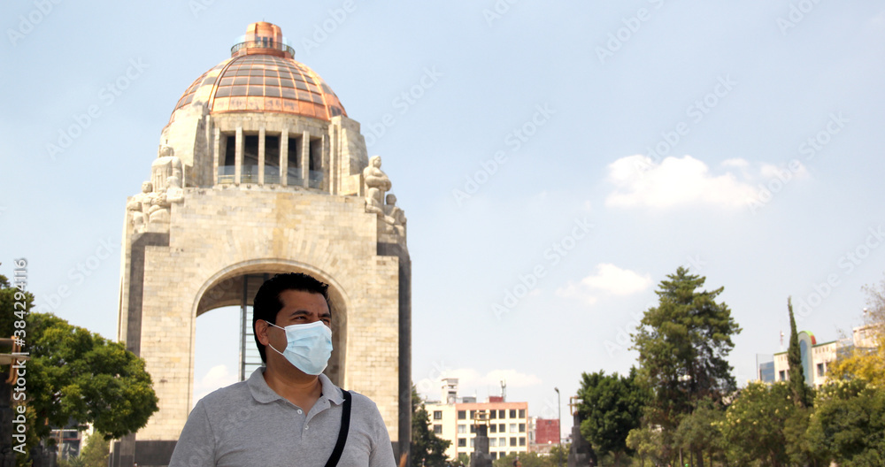 latin man with protection mask on street of mexico city with the new normal and the monument of the revolution in the background