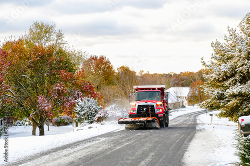 Canvas Print View of red truck with snowplow plowing suburban Midwestern street after first s