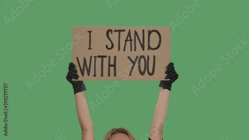 Blond woman holding over head a poster from a cardboard box with the words I STAND WITH YOU with both hands. Anti Black racism. Isolated a green screen, chroma key. Close up. Slow motion. photo