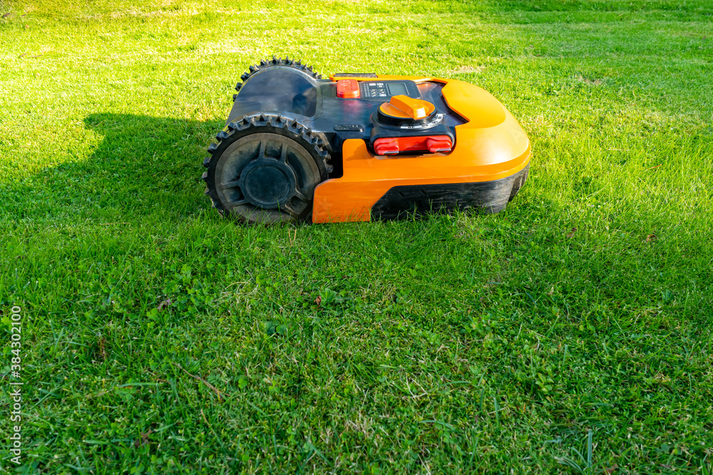 Side view of an orange robotic lawn mower on a green lawn cut by it Side view of an orange robotic lawn mower on a green lawn cut by it