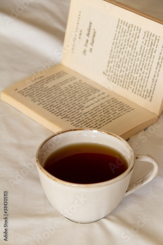 A cup of tea next to an open book on a white bed