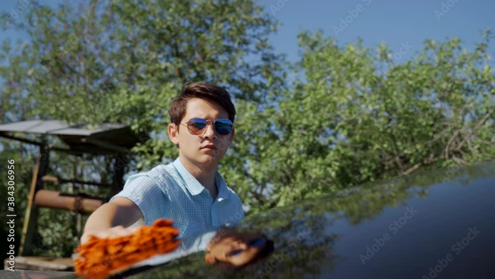A young man washes his car with a rag near the house on a sunny day. A young man washes his car with a rag near the house on a sunny day.