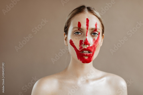 Portrait of girl with bare shoulders and red handprint on her face, looking at camera