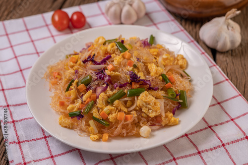 Stir fried glass noodles with eggs and put on a plate on a red white cloth.