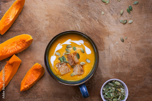 Pumpkin and carrot soup with cream on wooden background. Copy space. Top view.