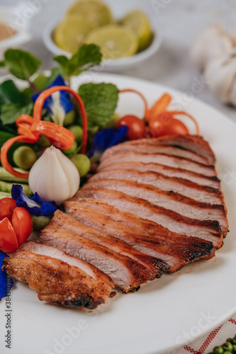 Sliced ​​fried pork with lemon, onion, red onion, tomato, long bean, butterfly pea flower, and mint.