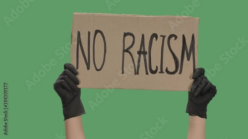 Female hands in black gloves pick up a poster from a cardboard box that reads NO RACISM. The concept of the global problem of racism in the world. Green screen, chroma key. Close up. Slow motion. photo