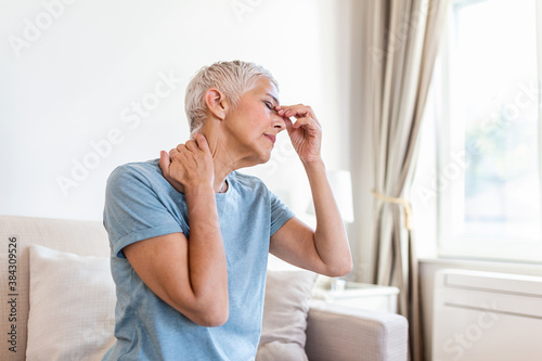 Woman suffering from stress or a headache grimacing in pain. Senior woman with migraine feeling unwell. Portrait of an attractive senior woman with a headache, feeling pain photo