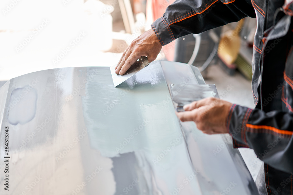 Repairing car body, Application putty close up. The mechanic repair the  car. Work after the accident by working sanding primer before painting.  Stock Photo
