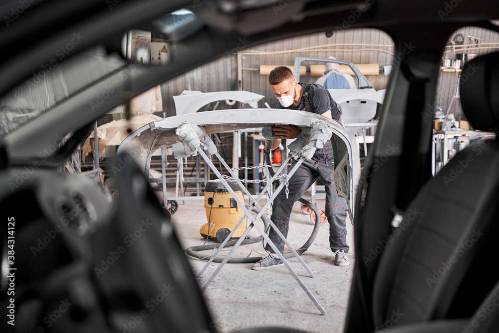 The mechanic works with a grinding tool. Sanding of car elements. Garage painting car service. Repairing car section after the accident. The mechanic works with a grinding tool. Sanding of car elements. Garage painting car service. Repairing car section after the accident.