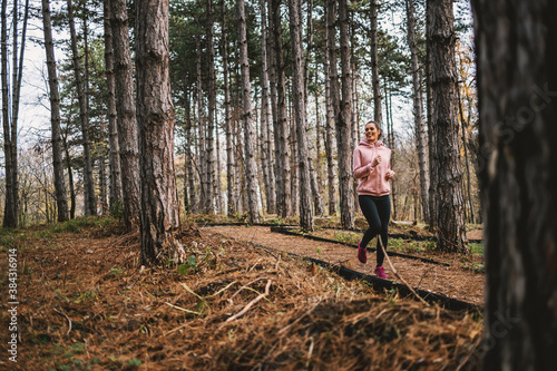 Young smiling sportswoman with healthy habits running in woods at autumn and preparing for marathon.