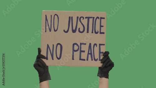 NO JUSTICE NO PEACE. Protest text message on cardboard. Stop racism. Police violence. Banner design concept. Hands in black gloves holding a poster a green screen, chroma key. Close up. Slow motion. photo