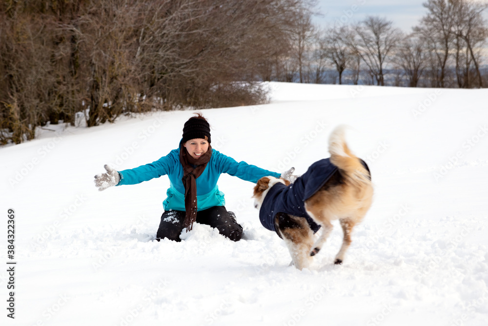 Dog is running to a happy young woman, snowy landscape at the winter season