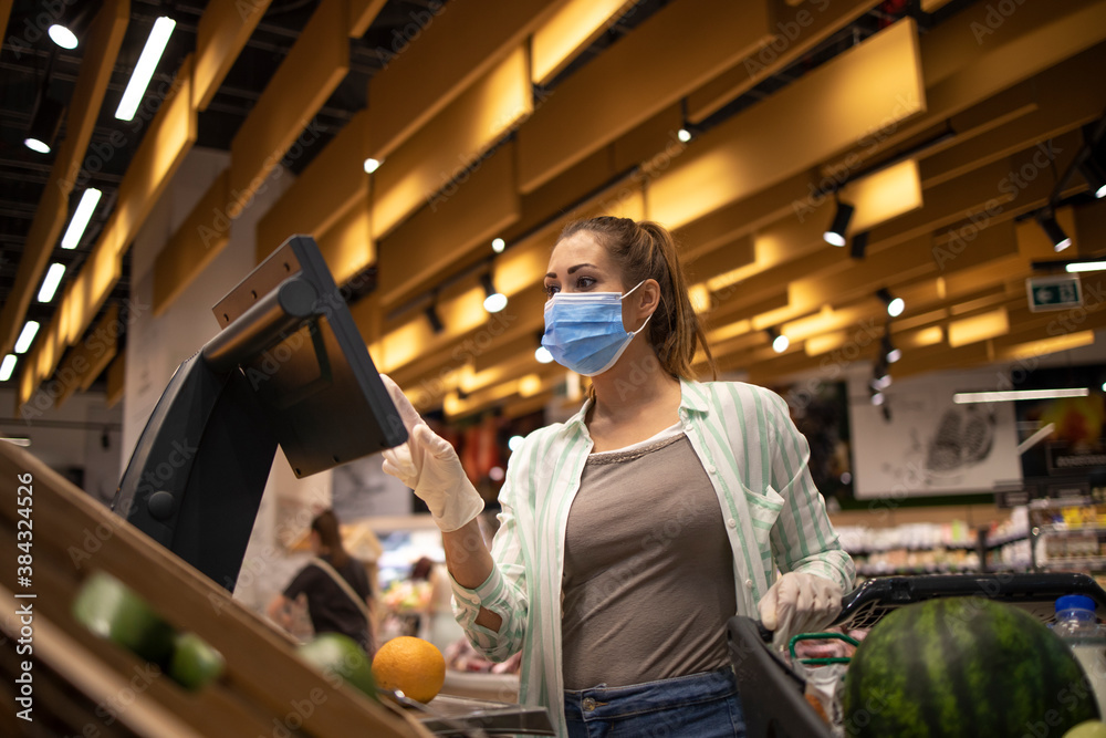 Buying food at supermarket during corona virus global pandemic. People wearing hygienic mask and gloves. Measuring food in grocery store and preparing for quarantine.