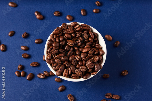Coffee Beans in white cup spilling over to the blue background 