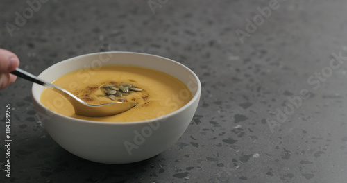 man eating pumpkin cream soup in white bowl on terrazzo countertop