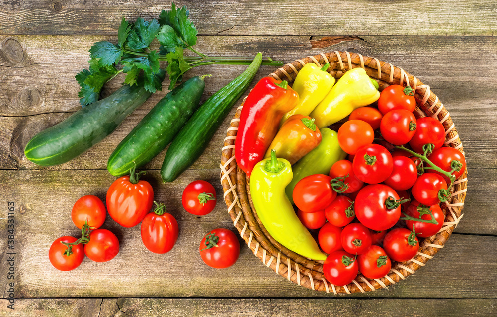 Harvest of fresh ripe vegetables on wooden table and in rod bowl - pepper, tomato, cucumber, celery leaves. Healthy organic food, summer vitamins, BIO viands, natural background. Top view