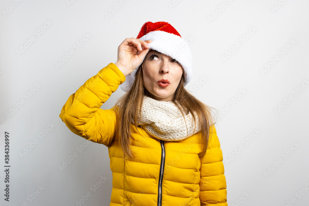 Young woman looks out from under Santa Claus hats wearing eyes on a light background. Concept of winter, winter holidays, Christmas, New Year. Funny mood, emotions, surprise, shock Young woman looks out from under Santa Claus hats wearing eyes on a light background. Concept of winter, winter holidays, Christmas, New Year. Funny mood, emotions, surprise, shock