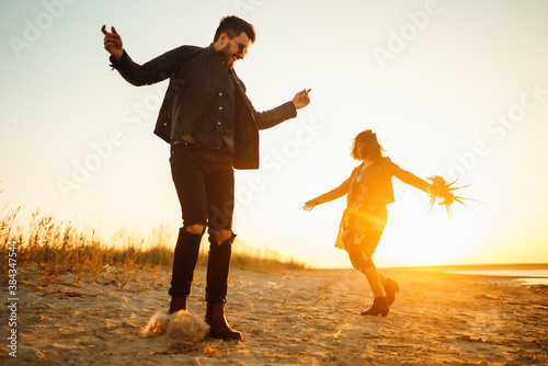 Stylish and loving couple enjoying each other by the sea at sunset. Romantic couple walk on the beach travel autumn vacation.