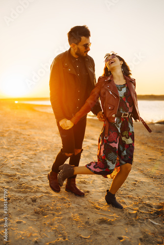 Stylish and loving couple enjoying each other by the sea at sunset. Romantic couple walk on the beach travel autumn vacation.