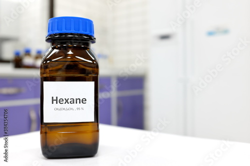 Selective focus of hexane liquid chemical compound in dark glass bottle inside a chemistry laboratory with copy space.  photo