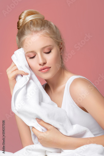 Closeup of woman cleaning skin with white towel. Portrait of beautiful blonde girl model wiping face skin with soft facial towel, removing makeup on a pink background. Studio shot. Skin care concept 