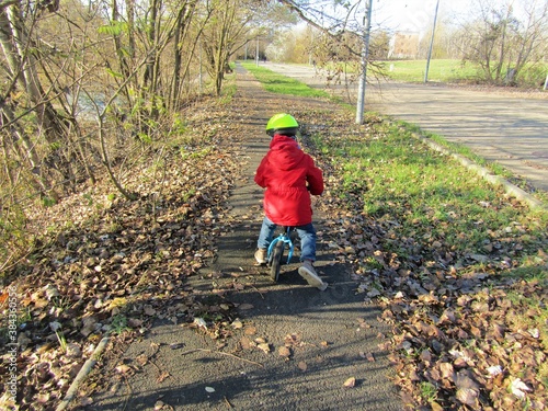 Little boy in red coat and yellow bike helmet riding a leg footed bike on an autumn road in Budapest green area  Hungary