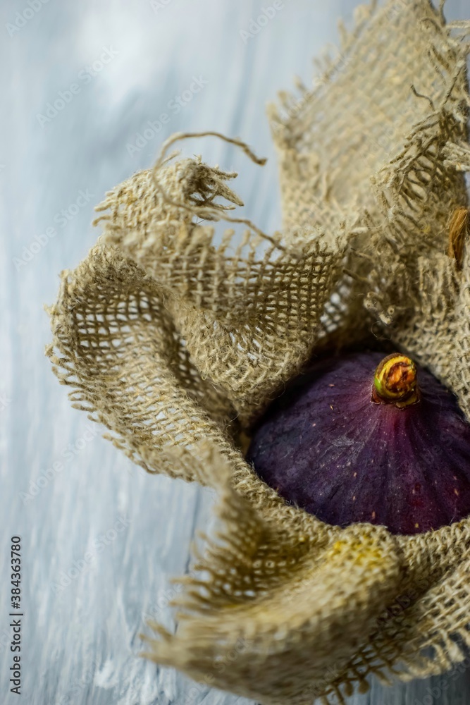 Fototapeta premium Bright purple luscious figs wrap in fabric on a gray wooden background. 