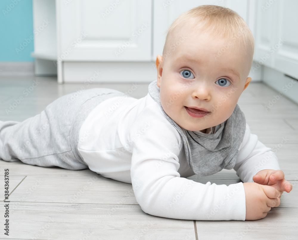 baby blonde boy with blu eyes in eco-friendly materials clothes is lying on the floor of the house. baby blonde boy with blu eyes in eco-friendly materials clothes is lying on the floor of the house.