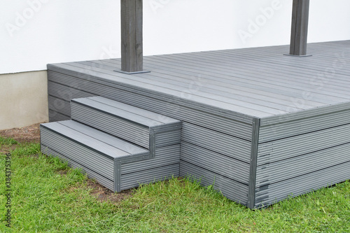 Part of dark gray or anthracite wpc composite meterial terrace deck with stairs  in backyard green grass outdoors. 