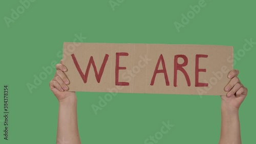 Hands hold a poster with the slogan WE ARE against the background of a green screen, chroma key. Stop Racism concept, No Racism. Close up. Slow motion. photo