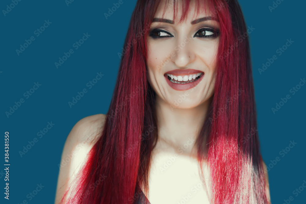 Fototapeta premium Portrait of happy charming red haired young woman wears looks to the camera, thinks and plans her birthday party isolated over blue background.evening make-up