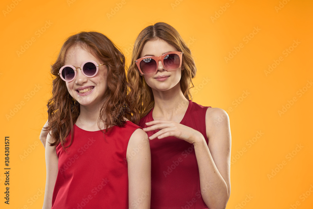 Happy woman and little girl in red dress are having fun on a yellow background fashion emotions sisters fun Copy Space. Happy woman and little girl in red dress are having fun on a yellow background fashion emotions sisters fun Copy Space.
