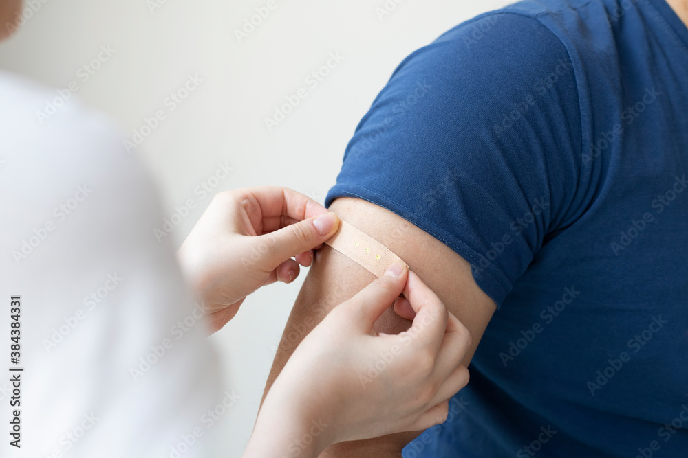 Woman applying adhesive bandage on man's arm against light background