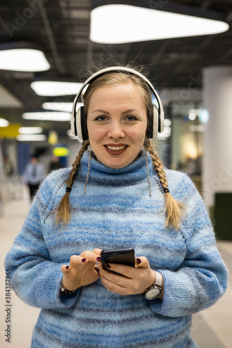 Portrait of a young smiling woman in headphones. a woman listens to music with headphones on her smartphone. © Регина Ерофеева