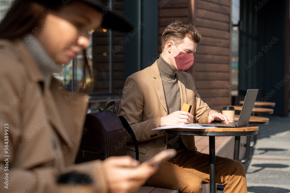Contemporary young elegant businessman in protective mask holding credit card Contemporary young elegant businessman in protective mask holding credit card