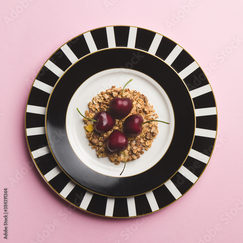 Top down view of four cherries in a bed of flakes, in black and white plates on a pink background