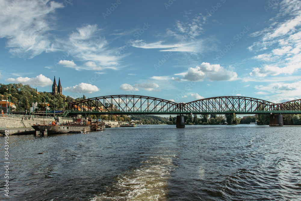 Postcard view of Vysehrad standing on massive rock looming over the Vltava river,Prague,Czech Republic.Czech national cultural monument.Riverfront houses,bridge,boats on sunny day.Sailing on river.