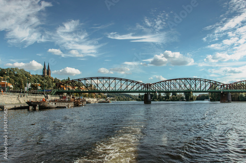 Postcard view of Vysehrad standing on massive rock looming over the Vltava river,Prague,Czech Republic.Czech national cultural monument.Riverfront houses,bridge,boats on sunny day.Sailing on river.