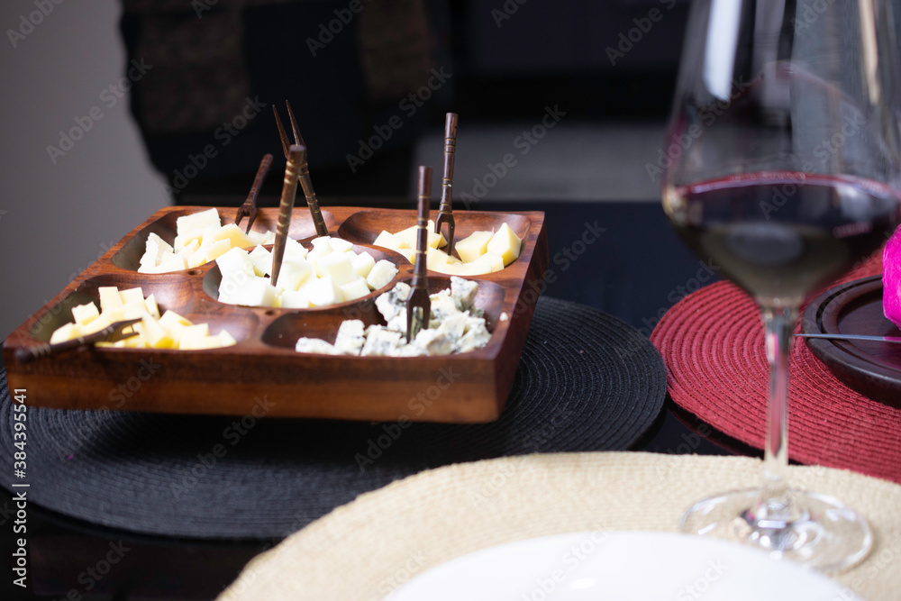 Wooden cheese board with gouda cheeses, fresh parmesan, parmesan and gorgonzola, served with red wine on a black topped table