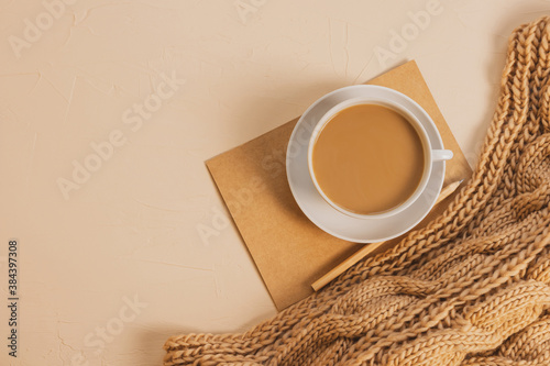 Cozy home flat lay: white cup with coffee, chunky knit scarf, notebook with pencil. The concept of the coming winter, christmas eve and new year. Warm shades, close-up.