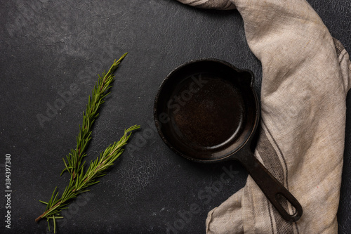 Empty black cast iron frying pan on a dark graphite background. Light linen towel. Fresh rosemary.