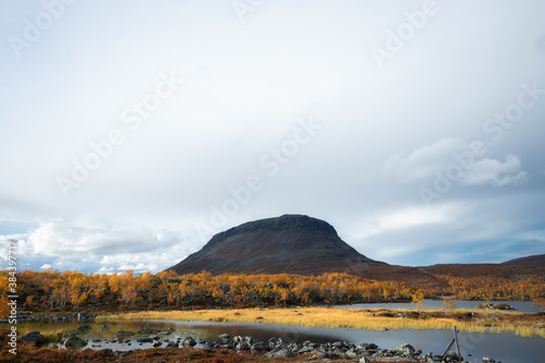 Beautiful autumn Lapland scenery. Saana mountain on background. Colorful yellow trees and small lake on foreground.